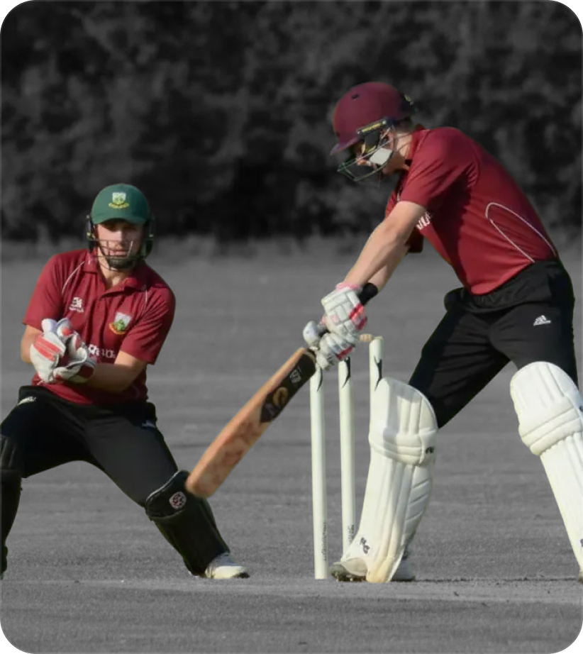 A male batter and male wicket-keeper in cricket club colours