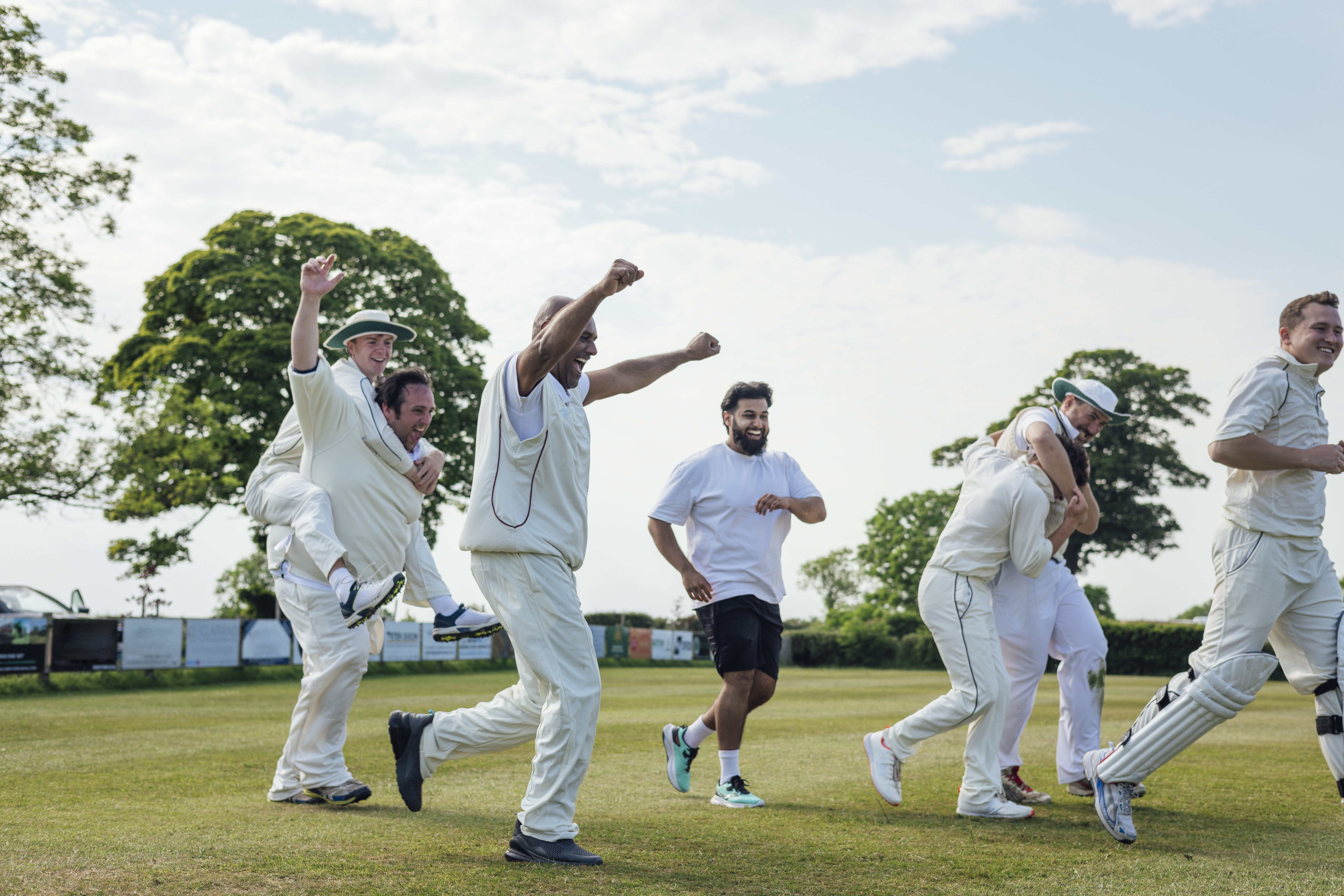 Seven recreational cricketers in whites running towards their teammates after a win