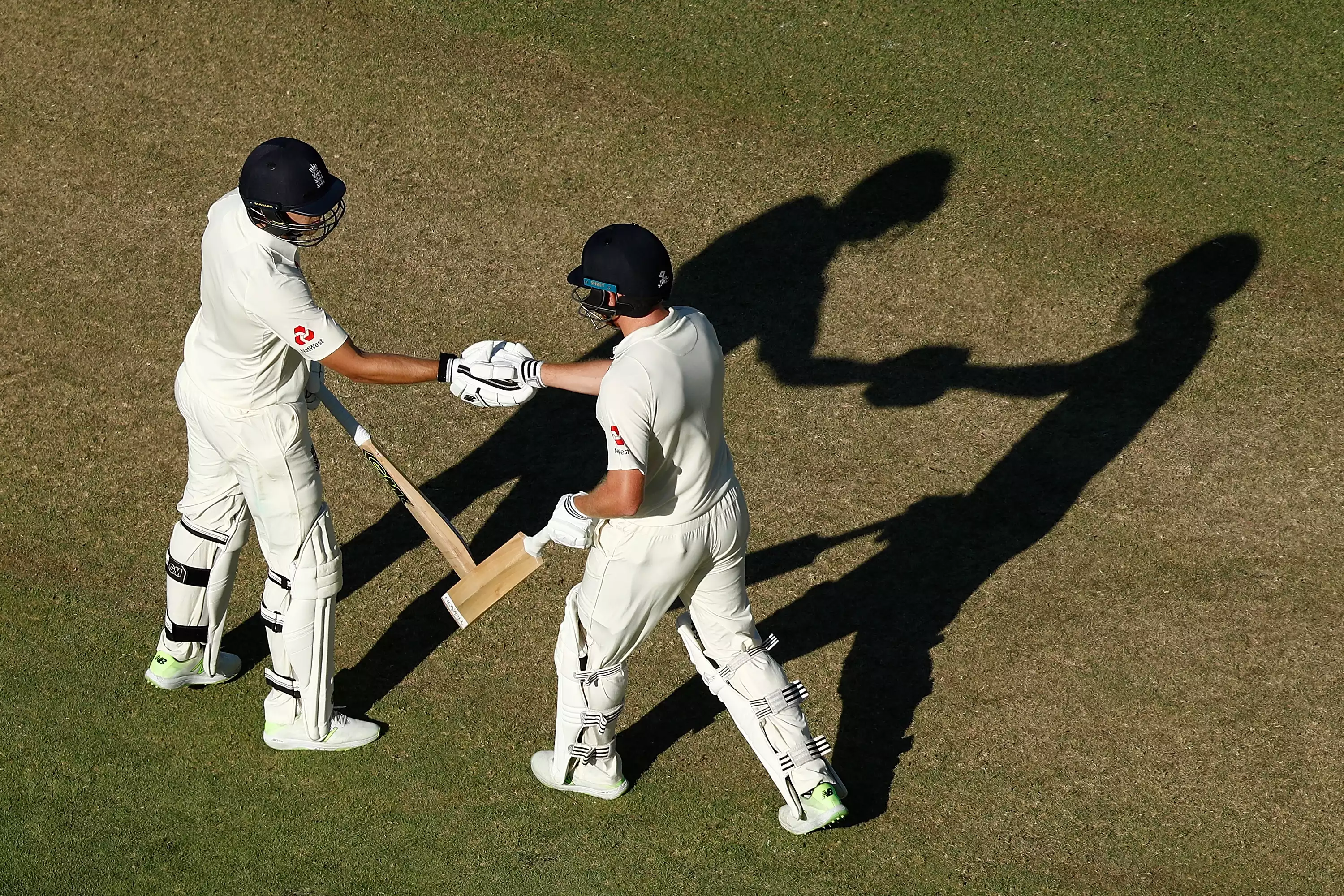Two male cricketers in club whites shaking hands